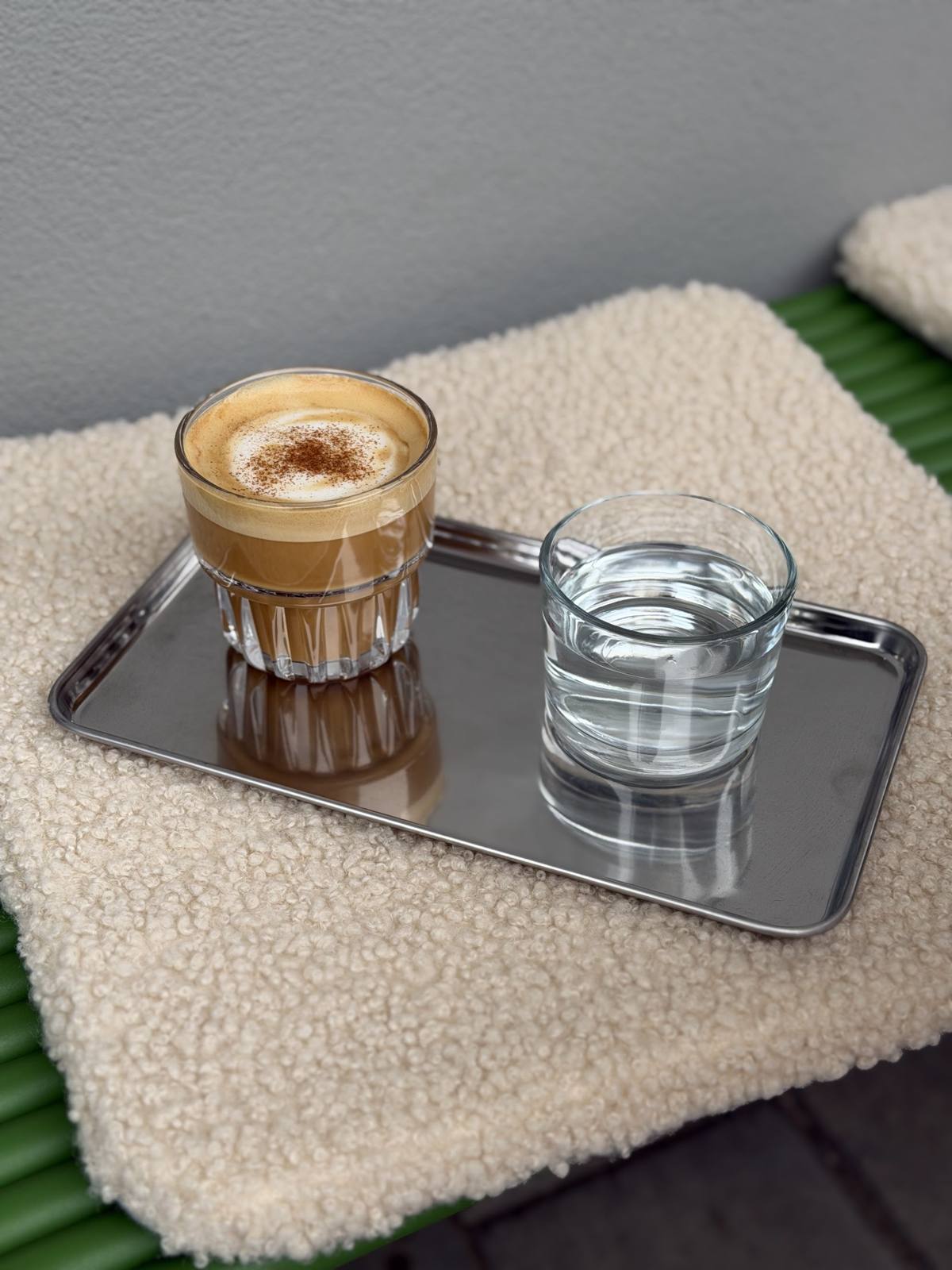 Cafea cu lapte într-un pahar de sticlă, pe o tavă, cu un pahar de apă alături