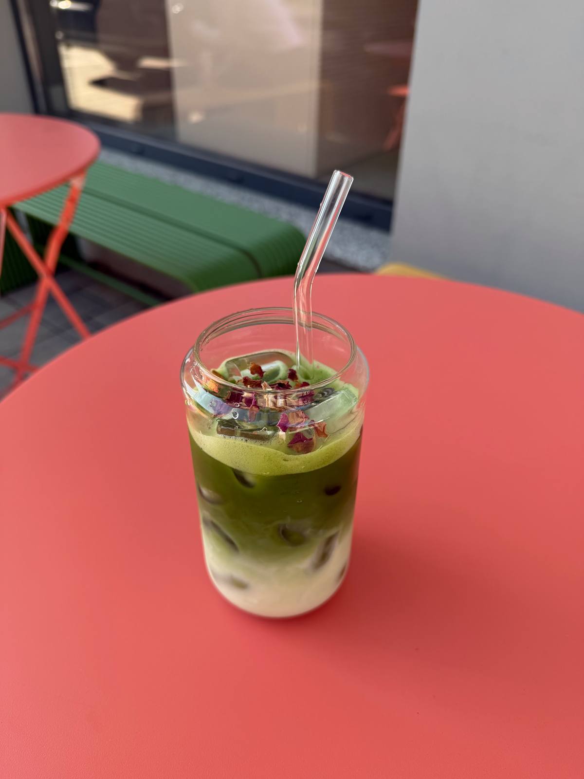Matcha latte cu gheață și petale de trandafir, pe o masă coral
